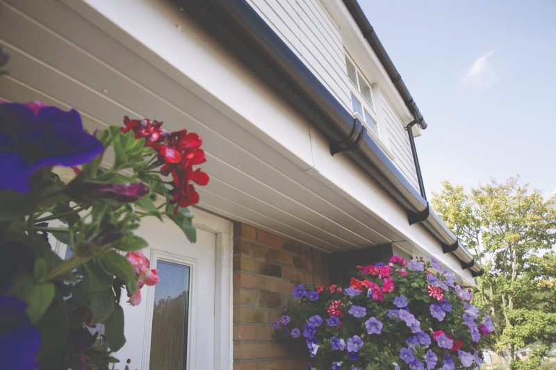 Close-up of white fascias and soffits with black guttering on Dorset home with hanging baskets of flowers